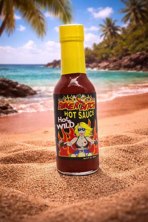 Biker Bitch hot sauce bottle on a sandy beach with palm trees and ocean in the background