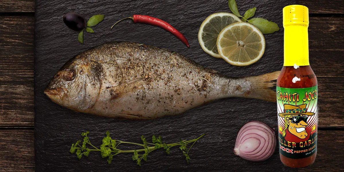 Dried fish on a slate surface with a bottle of hot sauce and garnishes.